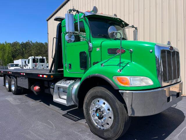 Green 2015 Peterbilt 348 rollback truck with flatbed, chrome bumper and dual rear axles, side mirrors, and stacked exhaust visible.