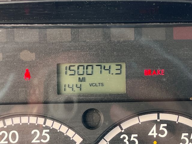 Dashboard display showing odometer reading 150074.3 miles and a 14.4 volts battery gauge in a Freightliner M2 cab. Brake warning light illuminated.