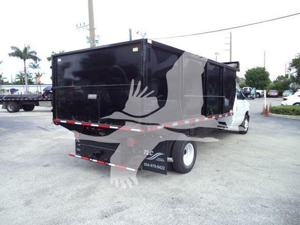 Dump truck body attached to a Ford E-450 chassis, black dump bed with red/white reflective tape, rear view showing license area and tires.
