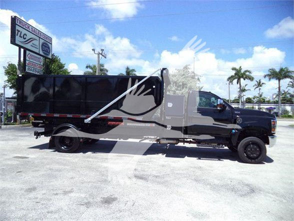 Truck with black dump bed and extended cab, side view, dealership sign in background. Text visible on the sign includes TLC Truck Sales Center. The vehicle has no obvious markings readable on the cab.