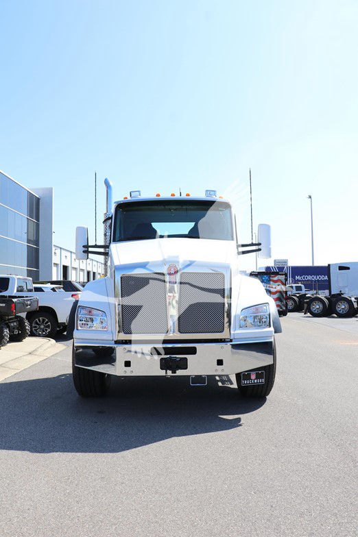 Kenworth T880 cab and chassis front view with large grille, chrome bumper, and tall exhaust stacks in a dealership lot.