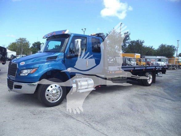 Blue International MV tow truck with flatbed trailer, front grille, dual exhaust, side tanks visible.