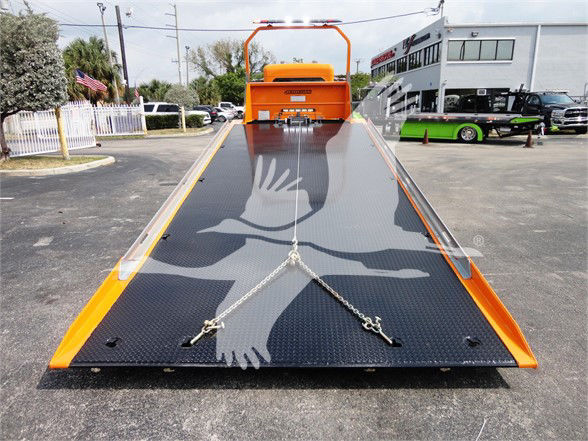Truck bed of a 2022 Peterbilt 337 tow truck with a black diamond plate flatbed and orange accents, parked in a lot.
