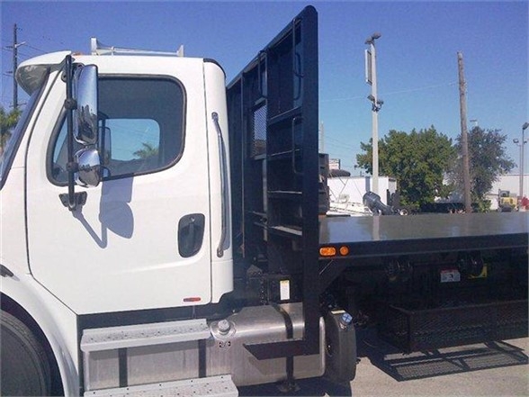Flatbed truck body side view showing white cab with black metal flatbed and rear metal ramp structure.