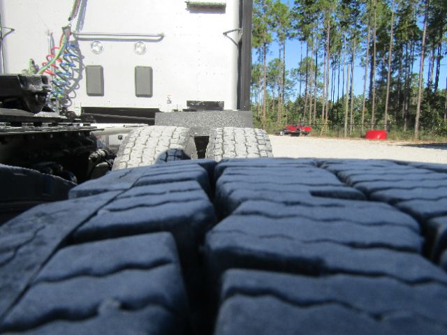 Rear view of a truck tractor chassis with large tires in foreground; some cab area and connectors visible in background.