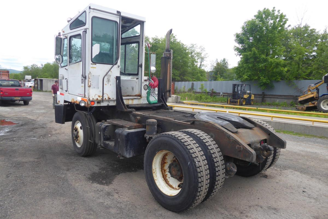 Truck tractor cab and chassis showing rear tires and fifth wheel, with rust and dirt on metal frame.
