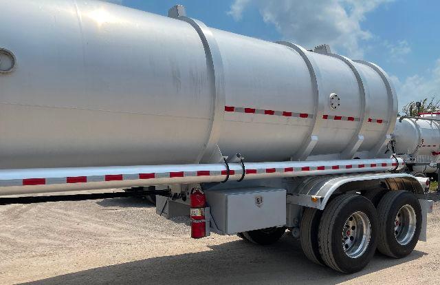 Aluminum DOT-407 crude oil tanker trailer, 200 barrel capacity, side view showing cylindrical tank, red and white reflective strips, dual rear axles, understructure, and a safety triangle.