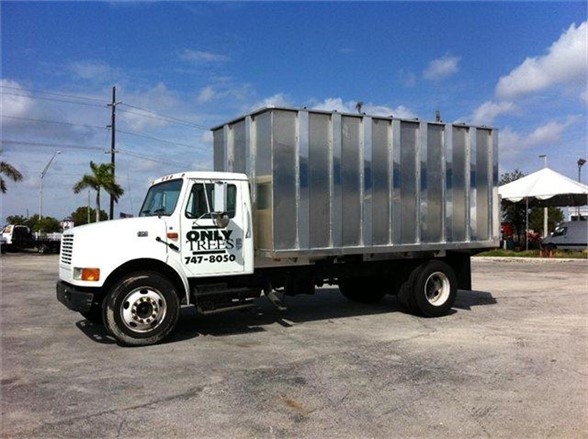 Dump truck with a galvanized dump body and white cab, side view showing storage bin on back.