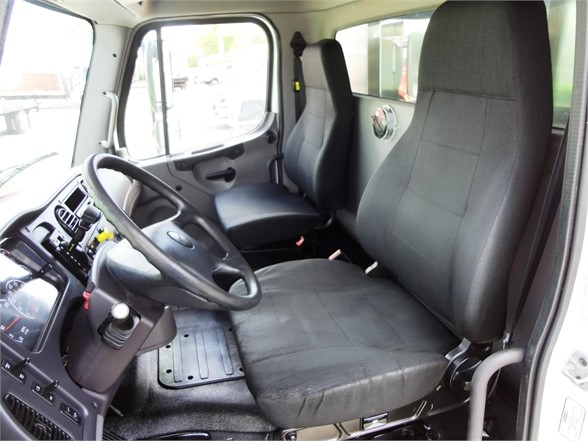 Cab interior of a Freightliner truck showing driver seat, passenger seat, steering wheel, and dashboard with controls.