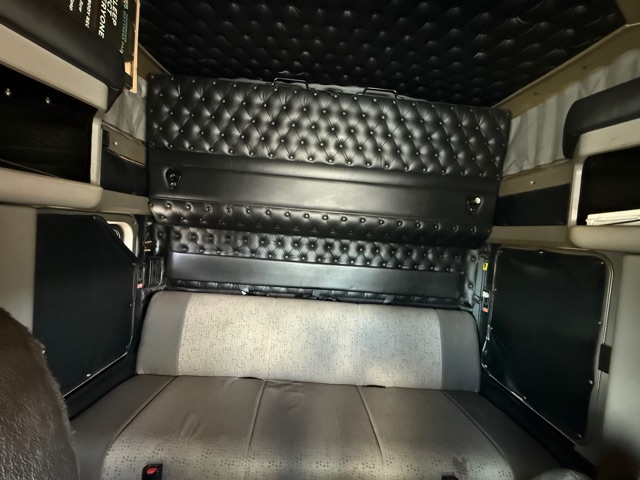 Interior of a 2012 Kenworth W900 sleeper cab showing black diamond-stitched upholstery on walls and bunk area.