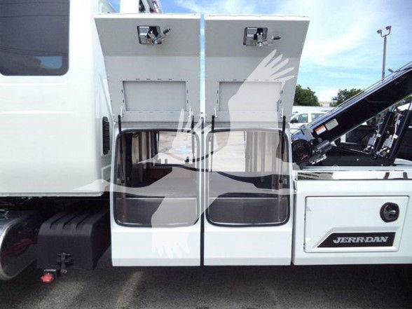 Two white truck doors open on a 2025 International MV cab, showing rear access with Men’s hand watermark overlay, JerrDan label on the side.