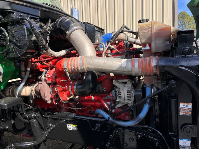 Peterbilt 579 engine bay showing red engine components, air intake hose, coolant reservoir, and alternator.