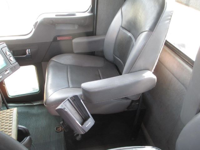 Kenworth T300 truck interior showing driver's seat with armrests and gray upholstery, floor mat, and control panel area.