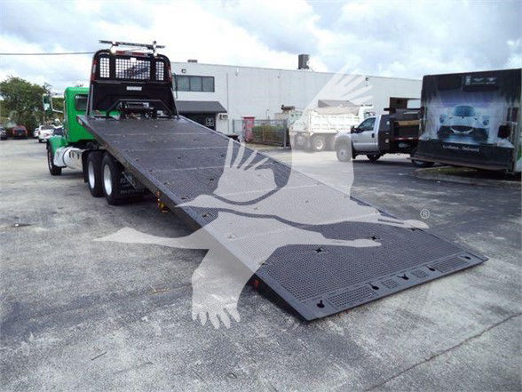 Peterbilt 367 tow truck with a long flatbed trailer in a parking lot.