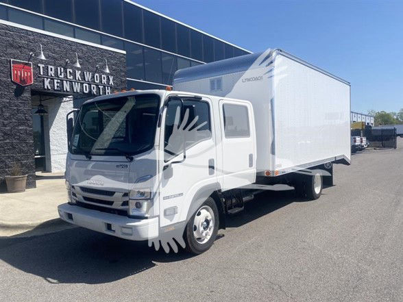 Isuzu NPR HD box truck in a dealership lot, front left view. Visible text includes 'ISUZU' on grille and 'TRUCKWORX KENWORTH' signage on building. No other legible labels observed on the truck itself.