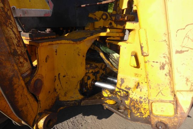 John Deere 710B backhoe truck equipment showing yellow body with exposed hydraulic cylinders and chassis components.