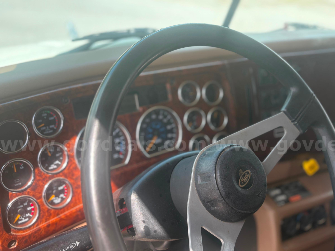 Vehicle interior showing Mack steering wheel and dashboard gauges in a 2002 Mack CV713 truck.