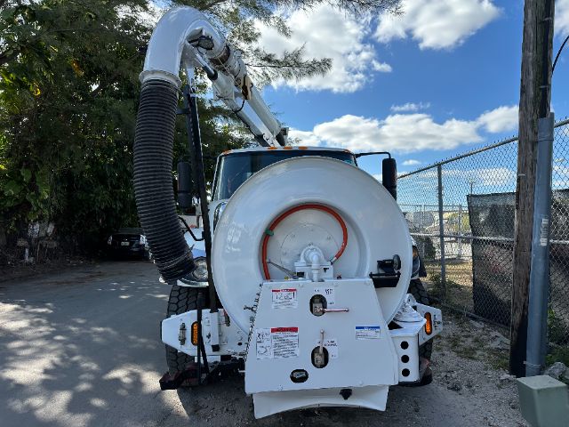 Vacuum truck rear showing circular tank and hose reel with rear controls and labels.