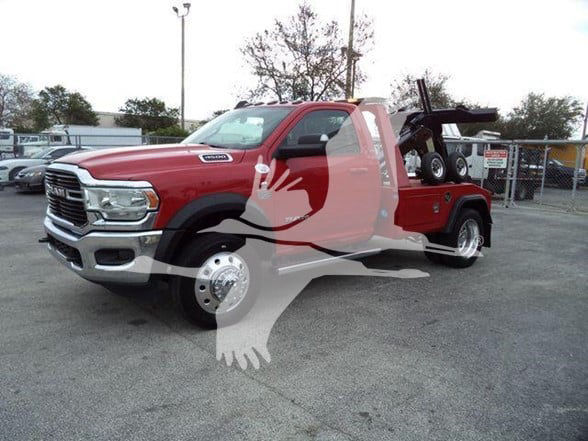 Tow truck with red cab and flatbed, Ram badge visible, front grille facing left, dealership lot in background.
