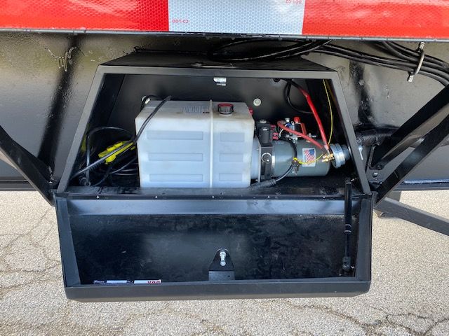 Crush car carrier trailer engine bay showing white coolant reservoir and auxiliary equipment inside open storage compartment.