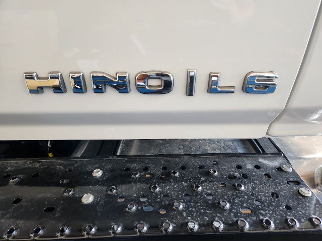 Hino L series cab and chassis emblem on side of white truck with perforated step and metal surface.
