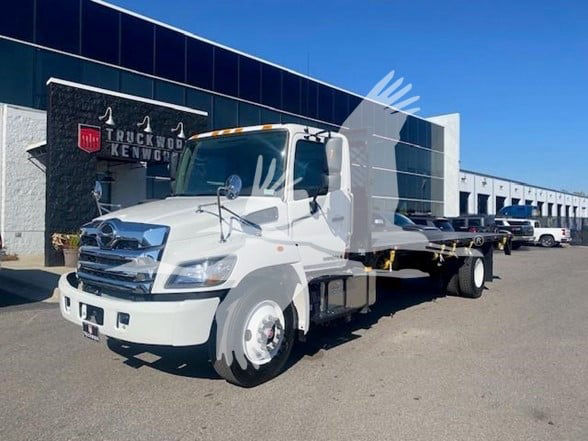 Front-left view of a white 2025 Hino flatbed truck parked outside a dealership.