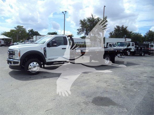 Ford F-550 tow truck cab in front of a flatbed, white color, with a long bed and towing setup, dealership lot in background.