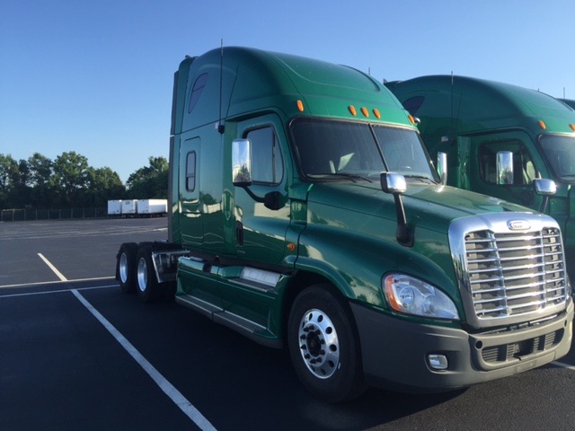 Green 2012 Freightliner Cascadia conventional sleeper truck in a parking lot, front grille visible, dual rear axles, chrome mirrors.