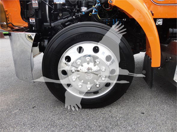 Peterbilt truck front wheel assembly with chrome hub and black tire, orange body panels visible, framework and hoses in background.