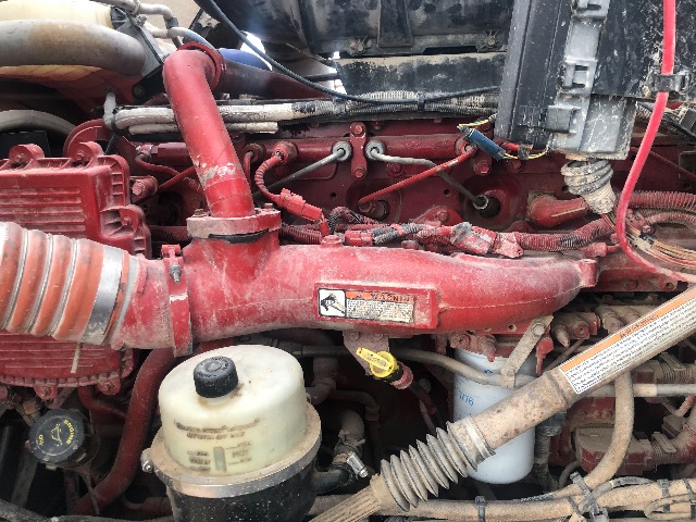 Kenworth T800 engine bay showing red intake manifold, yellow dipstick, white coolant reservoir, and various hoses and wiring.