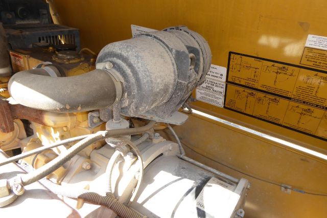 Trucking equipment engine bay showing a large belt-driven compressor and hoses, labeled with warning decals on a yellow panel.