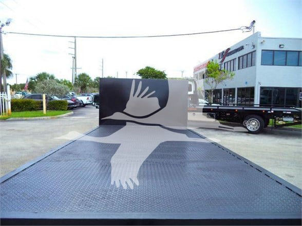 2011 Ford E450 stock image showing a flatbed with a large decorative dove graphic on the metal surface. Background includes a white building and other vehicles.