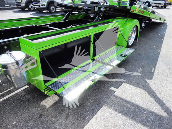 Green Peterbilt tow truck side step with chrome steps and black panels, fuel canister visible, large wheel and chassis in view.