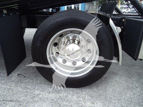 Freightliner Business Class M2 106 wheel/tire assembly showing chrome hub and lug nuts; part of heavy truck chassis with mudflap and wheel well visible.