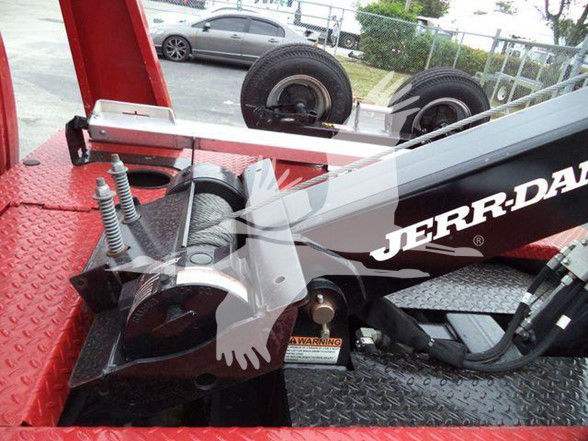 Tow truck bed with hydraulic arm and Jackson/ Jerry-? branding on black arm, visible warning label, chrome springs, diamond plate surface.