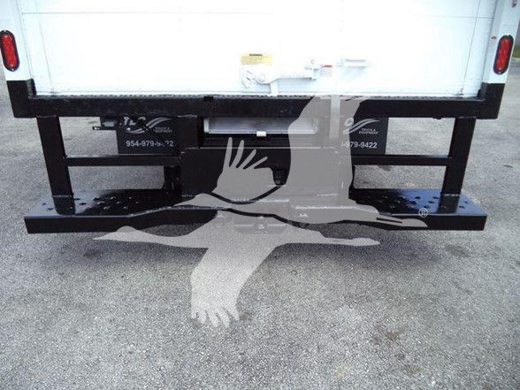 Rear of a Ford E-450 box truck showing a black steel bumper with two frame mounts and faint white text on the sides. The tailgate area is white.