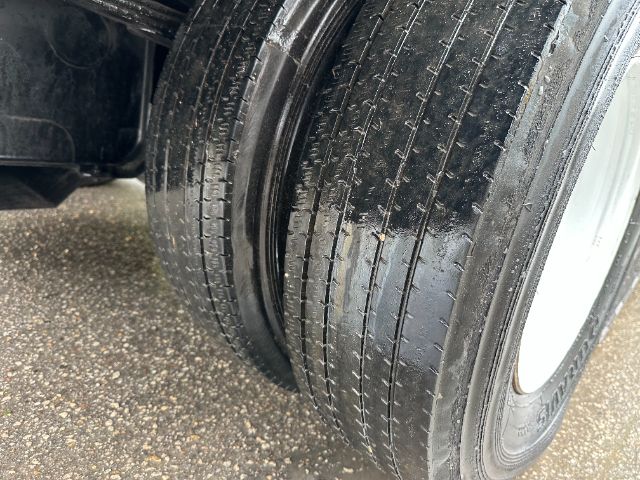 Isuzu NPR-HD sweeper truck front dual rear wheel tires visible, wet road surface, wheel rims, side of truck chassis.