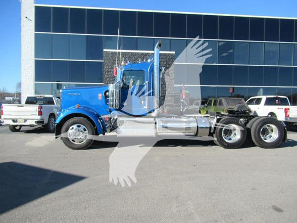 Blue Kenworth W900L conventional daycab truck with chrome fuel tanks and dual rear axles parked in front of a glass building.