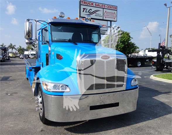 Blue 2022 Peterbilt 337 tow truck front view with large chrome grille and bumper, DOT light bar, and bright side mirrors.