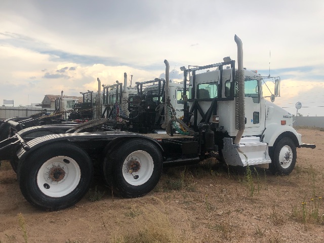 Kenworth T800 vacuum truck chassis with cab and dual rear axles, white cab, exposed exhaust stacks, side mirrors, and hydraulic equipment on frame.