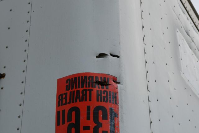 Van trailer side with a red warning sticker showing partial text '...H... FR... 3-P...' and riveted metal surface.