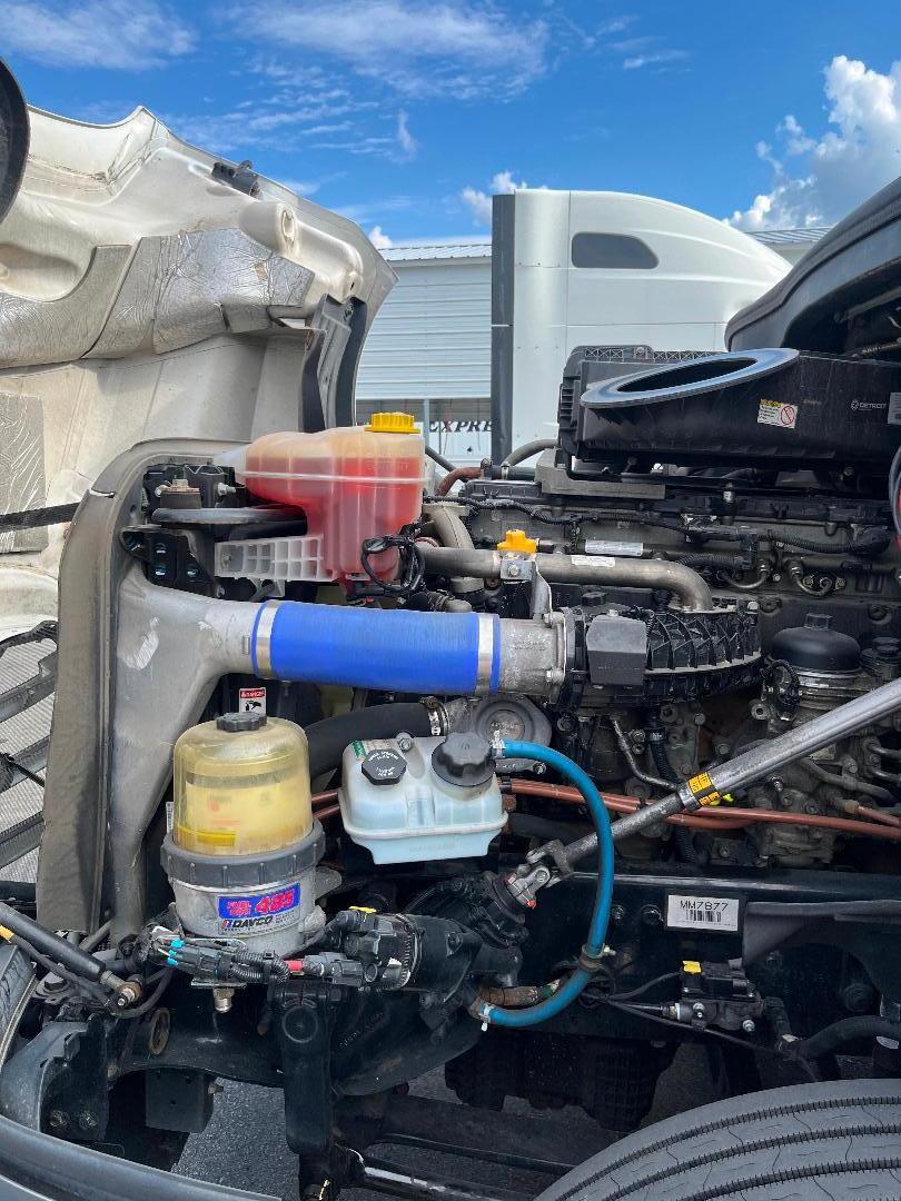 Front left engine bay of a 2021 Freightliner Cascadia 126 showing coolant reservoir, power steering/DEF containers, hoses, and radiator.