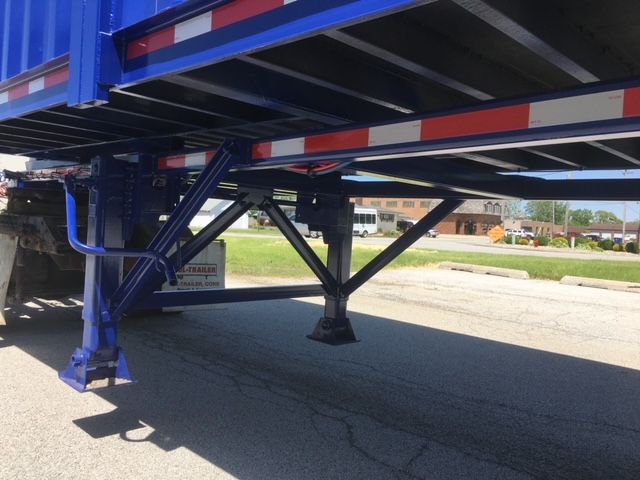 Blue and white 40 ft utility dump trailer undercarriage with support legs and frame, steel construction, and reflective red/white safety tape along the side.
