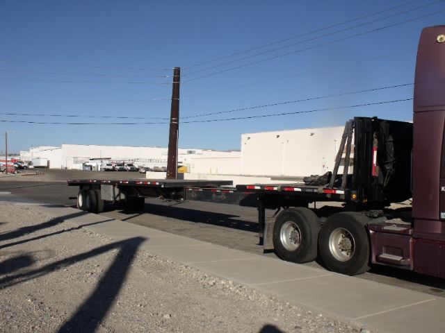 Flatbed trailer with extendable 48 to 80 foot section connected to a red semi-truck in a lot.