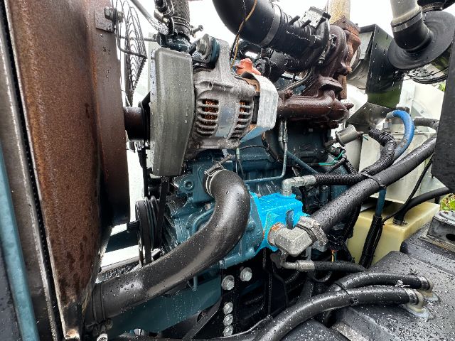 Isuzu NPR-HD engine bay showing blue engine block, alternator, belts, hoses, and radiator side with a yellow coolant reservoir.