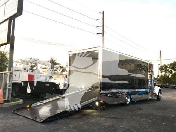 2022 Peterbilt 337 tow truck with a deployed ramp/loader in front, a large rectangular cargo box, and truck cab visible in background.