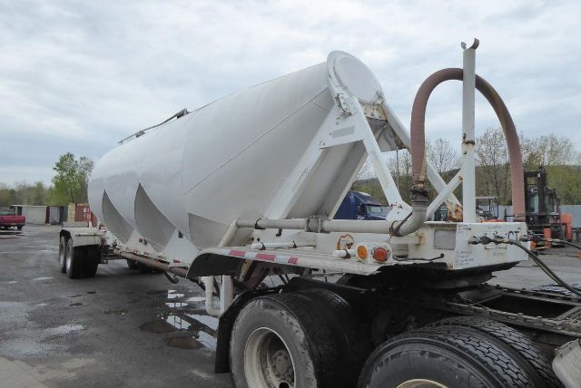 Fruehauf dry bulk trailer with cylindrical silo on a tractor-trailer unit, white paint, dual rear axles, piping and lift mechanism visible.