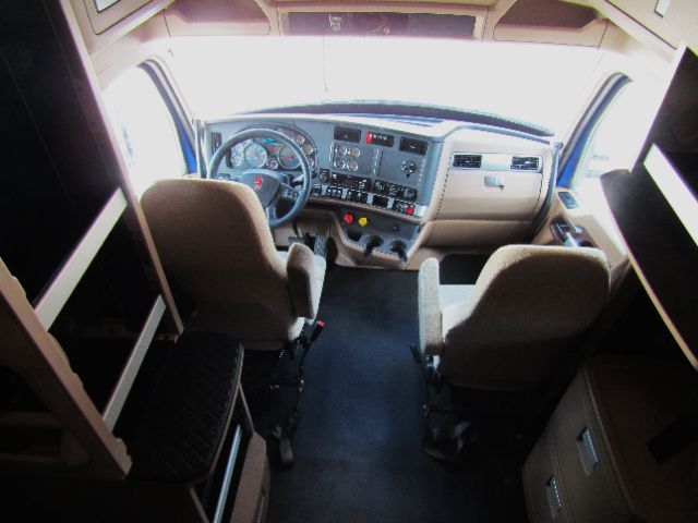 Kenworth T680 interior cab and dash viewed from back seats, steering wheel, dashboard controls and driver/passenger seats.