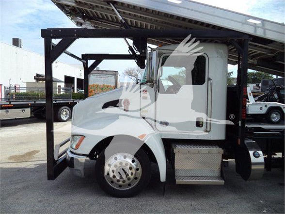 Kenworth T370 tow truck side view showing the cab and a hydraulic lift platform, white exterior, front wheel with chrome hubcap, and metal steps.