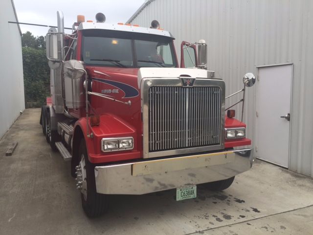 Truck front view of a red Western Star 4900FA conventional sleeper with chrome grille, large bumper, and green license plate; username tag on door; parking area.